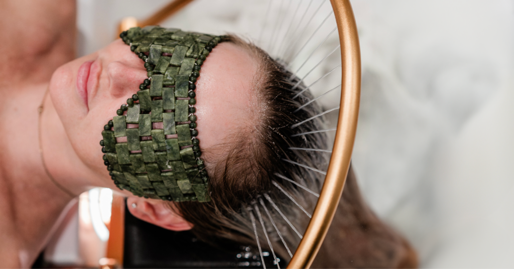 A female patient reclines on a treatment table with a jade eye mask, while a Salt Spa practitioner gently rinses her hair during a Japanese Head Spa treatment, creating a serene and relaxing atmosphere.